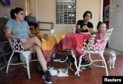 The couple made up of Gabriela Alfonso Pérez, 23, and Ria Acosta, 27, chat at a table in their garden together with Ria's daughter, Ivelle Acosta, 2, in Havana, Cuba, on July 13 of 2022.