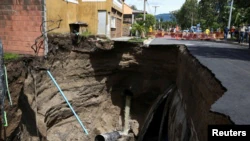 Workers stand next to a collapsed street after a flood caused by heavy rains, after tropical storm Bonnie, in San Salvador, El Salvador, July 3, 2022. REUTERS/Jose Cabezas