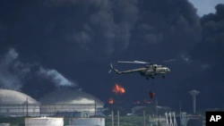 A helicopter drops water on the Matanzas supertanker base, as firefighters try to douse a fire that started during a thunderstorm the night before, in Matazanas, Cuba, Saturday, Aug. 6, 2022. Cuban authorities say lightning struck over a crude oil storage tank on the base, sparking a fire that caused four explosions that injured more than 70 people.  (AP Photo/Ramon Espinosa)