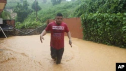 A man walks through a street flooded by Hurricane Fiona in Cayey, Puerto Rico, Sunday, Sept. 18, 2022. (AP Photo/Stephanie Rojas)