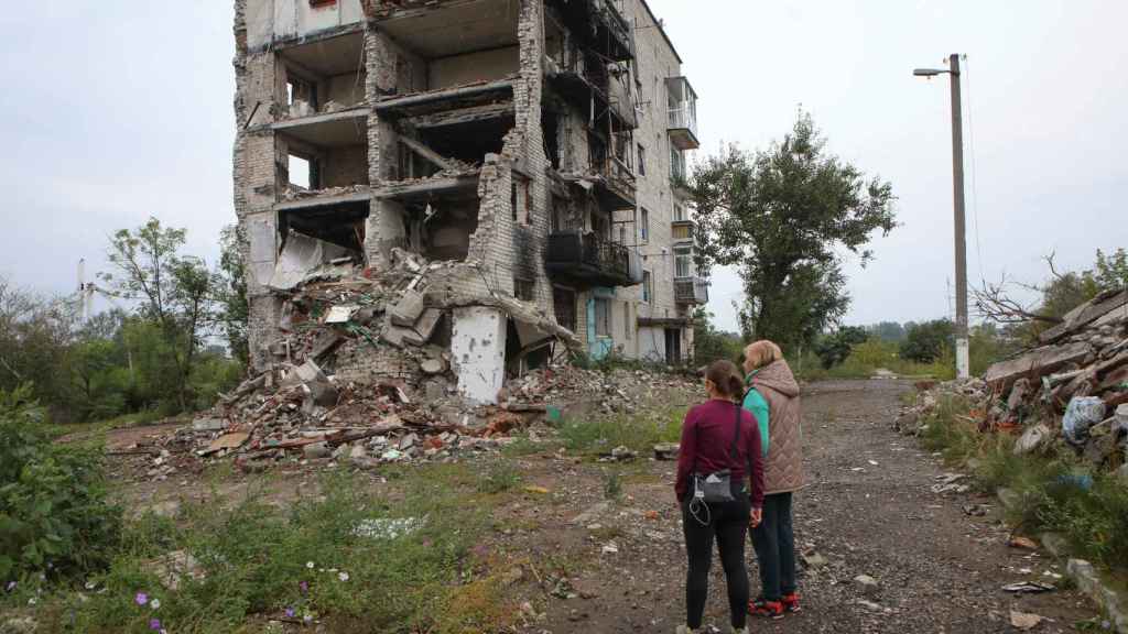 The women stand near a residential building destroyed by a military attack in the city of Izium.