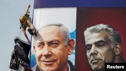 FILE - A worker hangs a Likud party election campaign banner depicting the party's leader Israeli Prime Minister Benjamin Netanyahu and his rival Yesh Atid party leader Yair Lapid in Jerusalem on 11 March. March 2021.