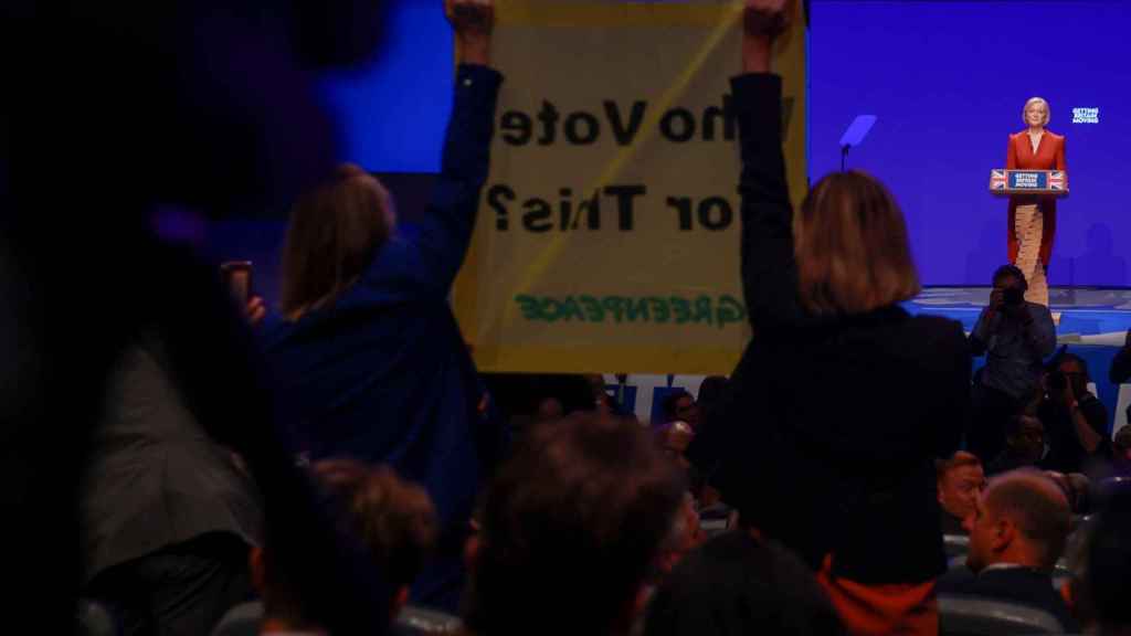 Greenpeace activists stand before Truss with a banner: 'Who voted for this?'