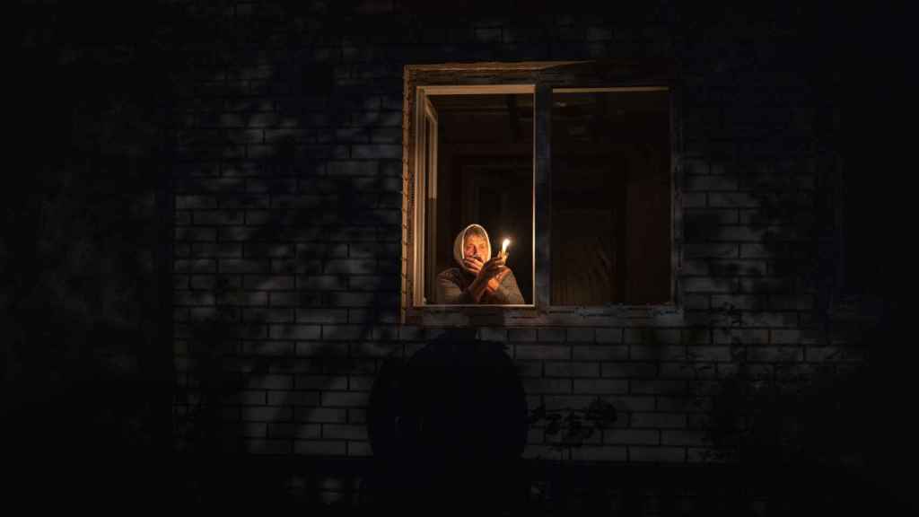 A woman lights a candle in her unlit house in the kyiv region after a wave of Russian missile attacks.