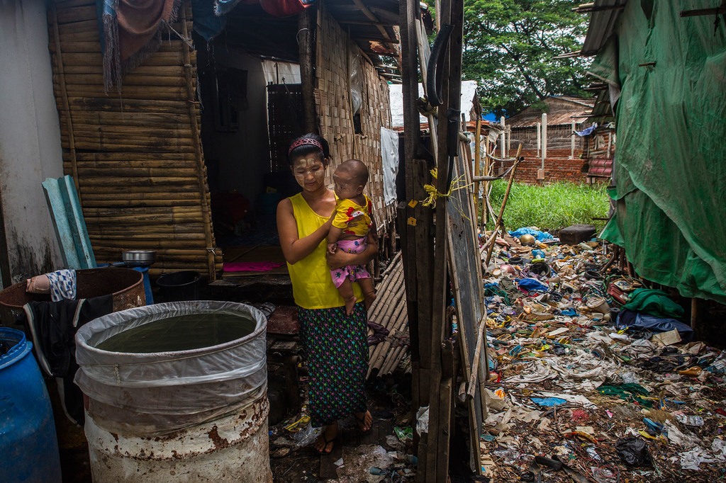 the cost of living crisis its citizens are currently facing and will magnify inequalities around the world.  Pictured, A woman holds her six-month-old son in front of her small makeshift home in Yangon, Myanmar.