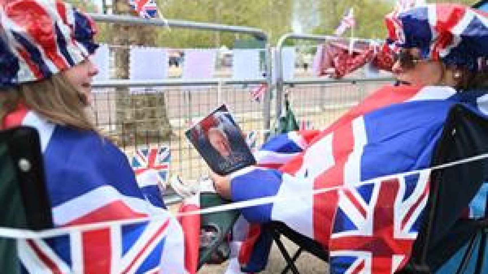 Royal fans read a book about King Charles as they wait on the coronation procession route on The Mall in London, Great Britain, on May 05, 2023.