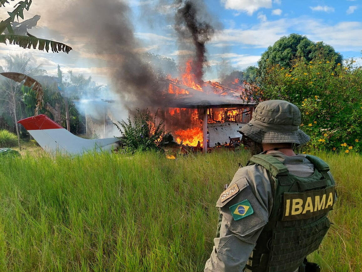 An agent from the Brazilian Institute for the Environment and Renewable Natural Resources (IBAMA) watches as a plane and a miners' house are destroyed during a joint operation with other state agencies.