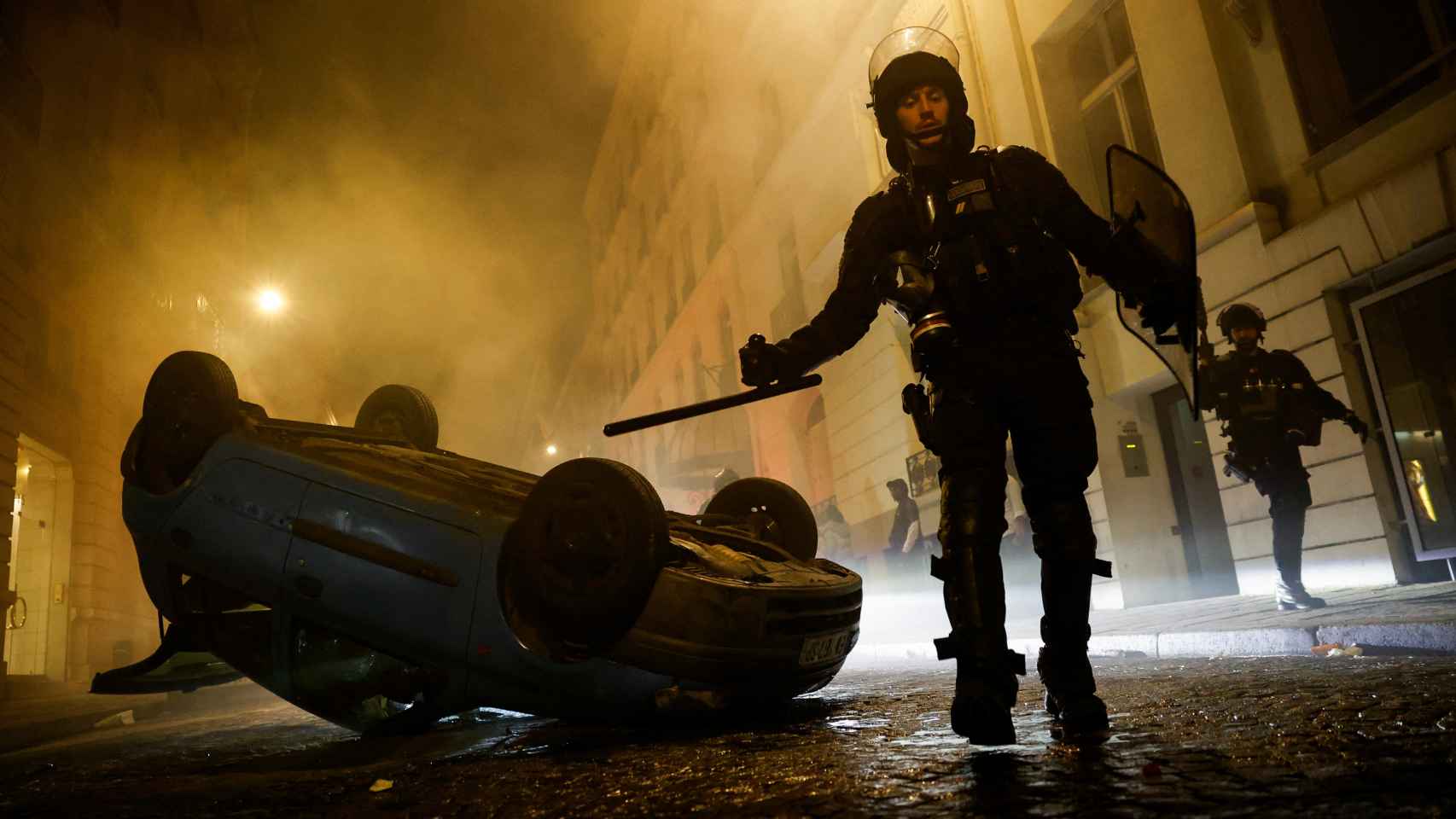 A police officer walks past an overturned car in Paris during riots.