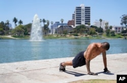 A man exercises shirtless as temperatures rise in MacArthur Park, Tuesday, July 11, 2023, in Los Angeles.  Los Angeles is expecting high temperatures between 100 and 110 degrees Fahrenheit later this week according to the National Weather Service.  (AP Photo/Marcio José Sánchez)