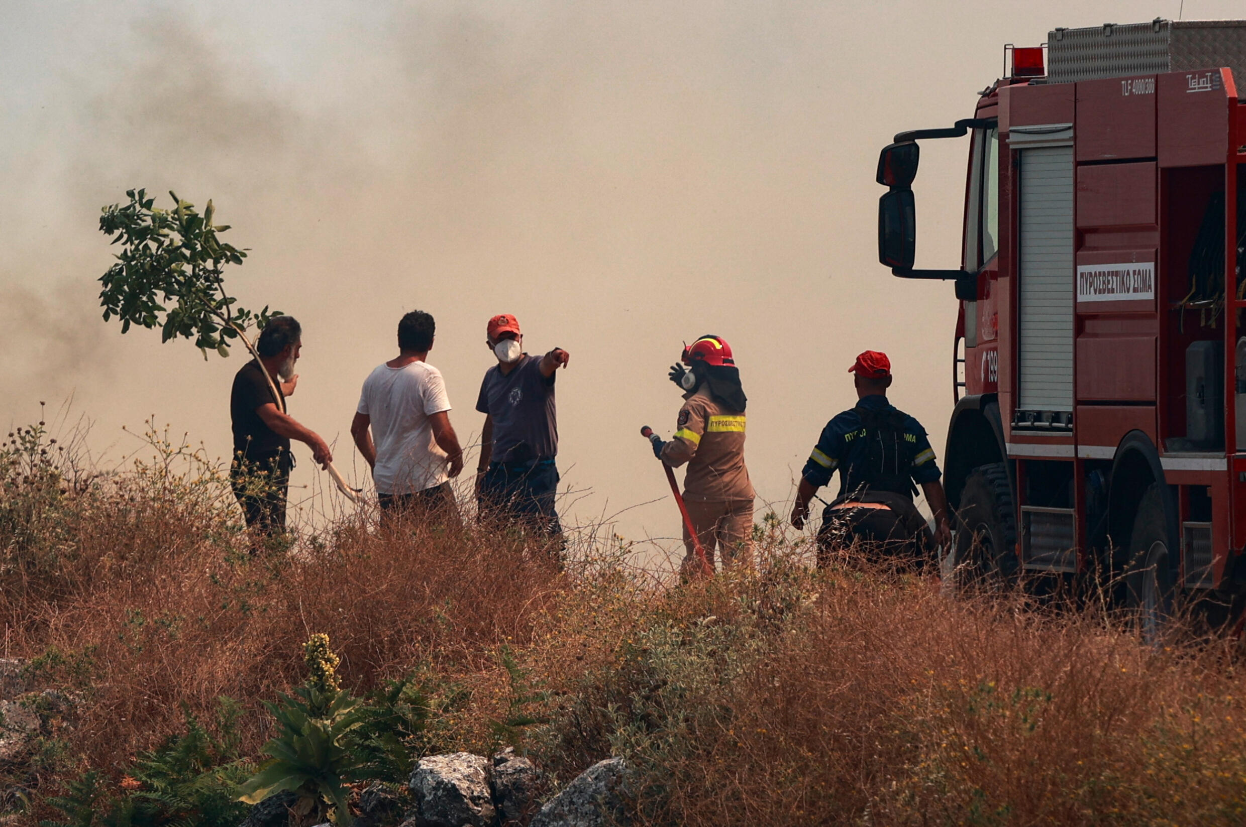 Firefighters and civilians face plumes of smoke as wildfires burn, in the northern part of the Greek island of Corfu, on July 24, 2023.