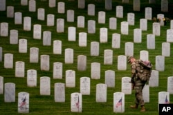 FILE - A member of the 3rd US Infantry Regiment places flags in front of each headstone to "Flags-In" at Arlington National Cemetery in Arlington, May 25, 2023, to honor the nation's fallen military heroes ahead of Memorial Day.