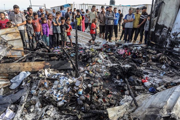 A group of Palestinians stand next to burned tents in a displaced persons camp in Rafah, in the Gaza Strip.