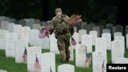 A U.S. Army Old Guard soldier places a flag on a headstone during the annual 'Flags In' event, ahead of Memorial Day at Arlington National Cemetery in Arlington, Virginia, May 23, 2024.