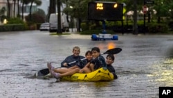 Matthew Koziol, Matías Ricci, Manuel Ricci and Raúl Fernández travel by raft through a street flooded by heavy rain on North Bay Road in Sunny Isles Beach, Florida, on Wednesday, June 12, 2024