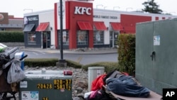 A person leaves a KFC fast food restaurant as another homeless person sleeps at the busy intersection of Oregon Coast Highway and 5th Street on June 19, 2024, in Brookings, Oregon, USA.