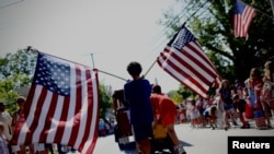 A boy carries American flags through Barnstable Village on Cape Cod, during the annual Fourth of July parade celebrating the country's Independence Day, in Barnstable, Massachusetts, U.S., July 4, 2024.