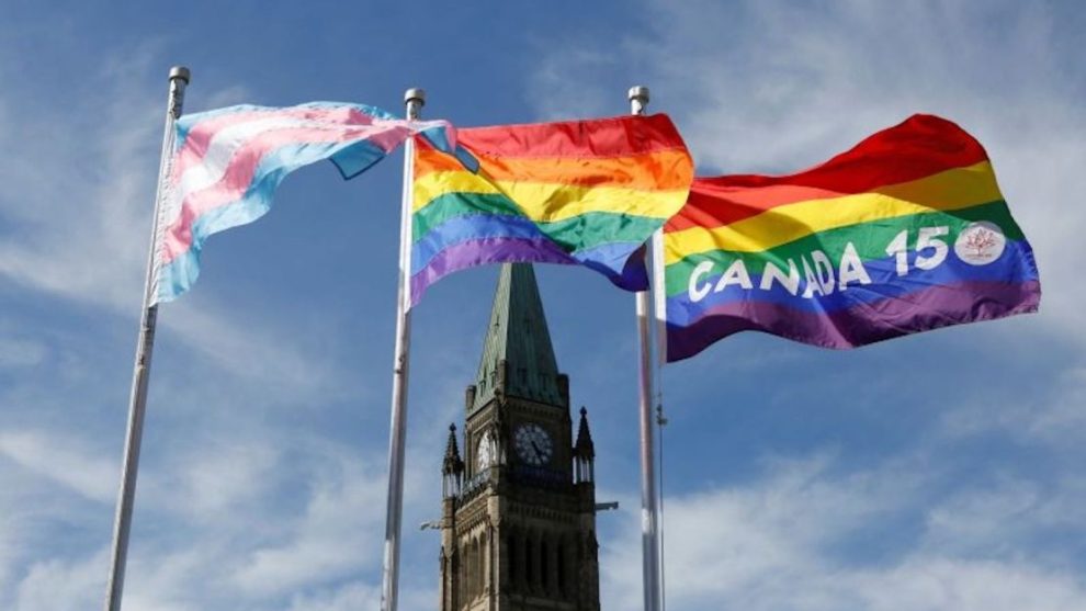 Transgender pride flags, left, gay pride flag, center, and the 150 Years of Canada Pride flag wave after a flag ceremony on Parliament Hill in Ottawa, Canada, June 14, 2017.