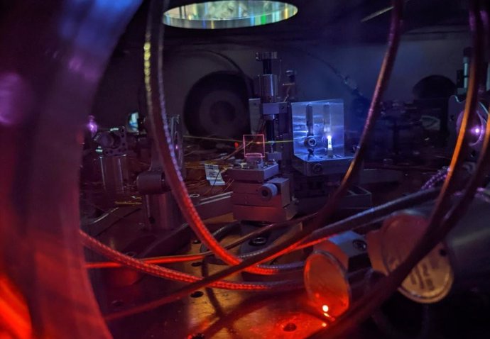 A powerful laser shines on a jet of gas, creating a glowing plasma and generating ultraviolet light. The light leaves a visible white line as it interacts with the remaining gas in the vacuum chamber.