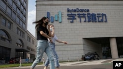 FILE - In this Aug. 7, 2020, file photo, women wearing masks to prevent the spread of the coronavirus chat as they walk past the headquarters of ByteDance, owners of TikTok, in Beijing, China.