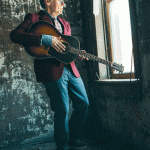 John Hiatt holds a guitar while looking out the window. (Courtesy photo)