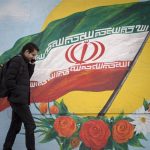 File - February 17, 2020, Tehran, IRAN: Iranians walk next to a wall painting of the Iranian national flag in Tehran, Iran. Many Iranians, battered by economic sanctions, political turmoil and the lingering threat of military conflict, say they are in