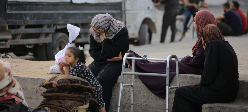 Women who have fled their homes in Gaza rest on a wall.