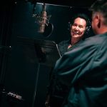 Wayne Newton in black jacket and headphones recording vocals for the song 'This Is America' next to a microphone