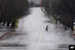 A pedestrian walks down a rain-soaked street in Dallas, Thursday, Dec. 26, 2024. (AP Photo/LM Otero)