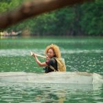 Mel B in a boat, rowing in the middle of a mass of sea.